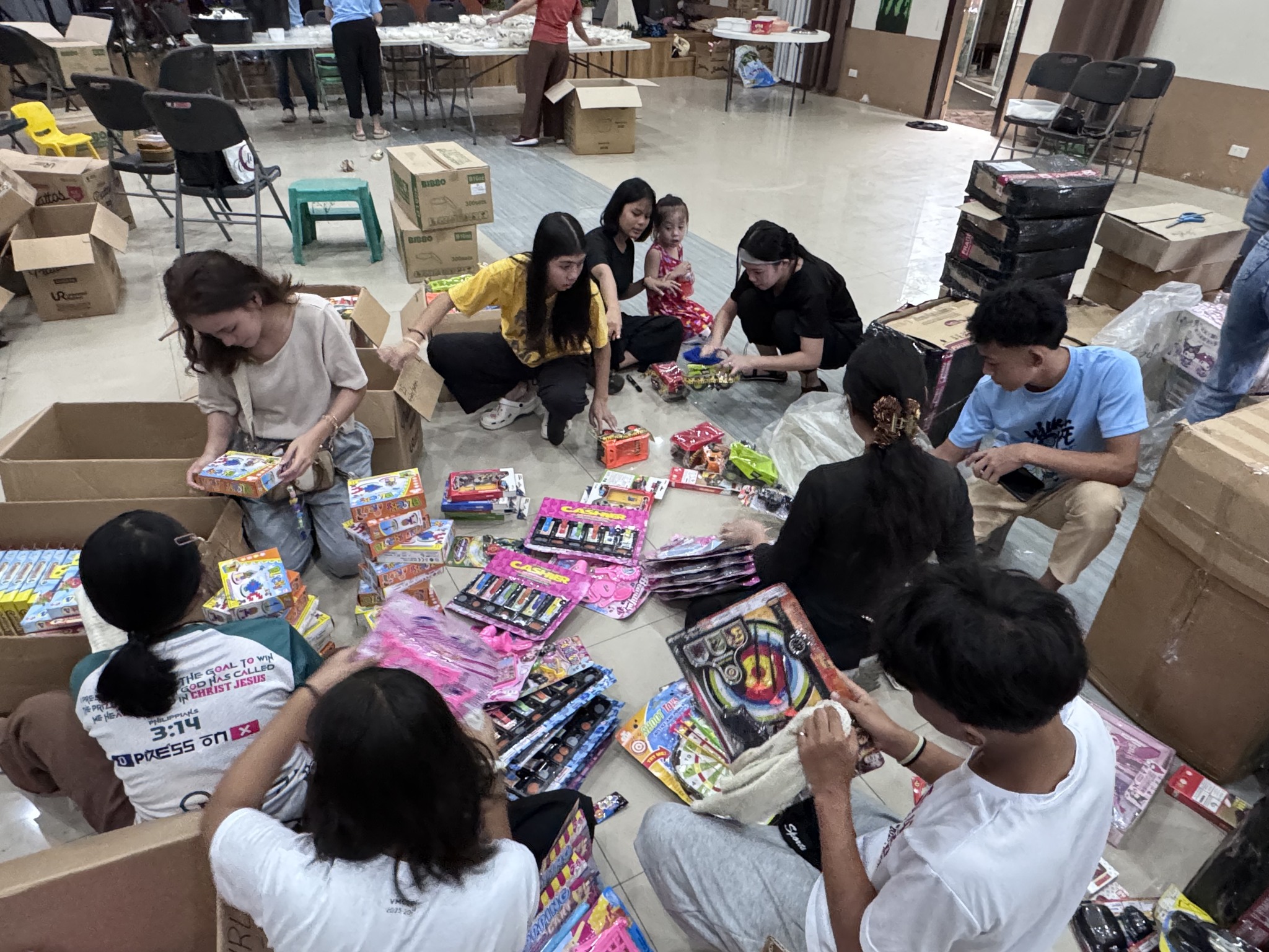 Volunteers sitting on the floor sorting toys and gifts into bags for the children