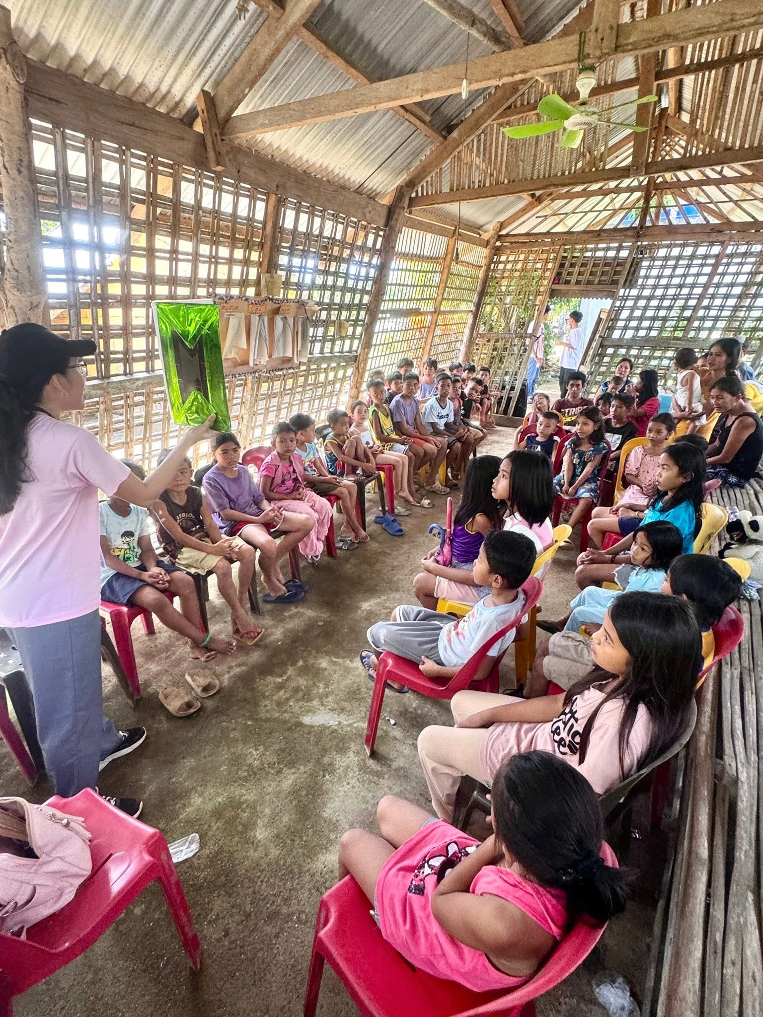 A teacher shares a Bible story with dozens of children seated inside a community hall in Masbate Province