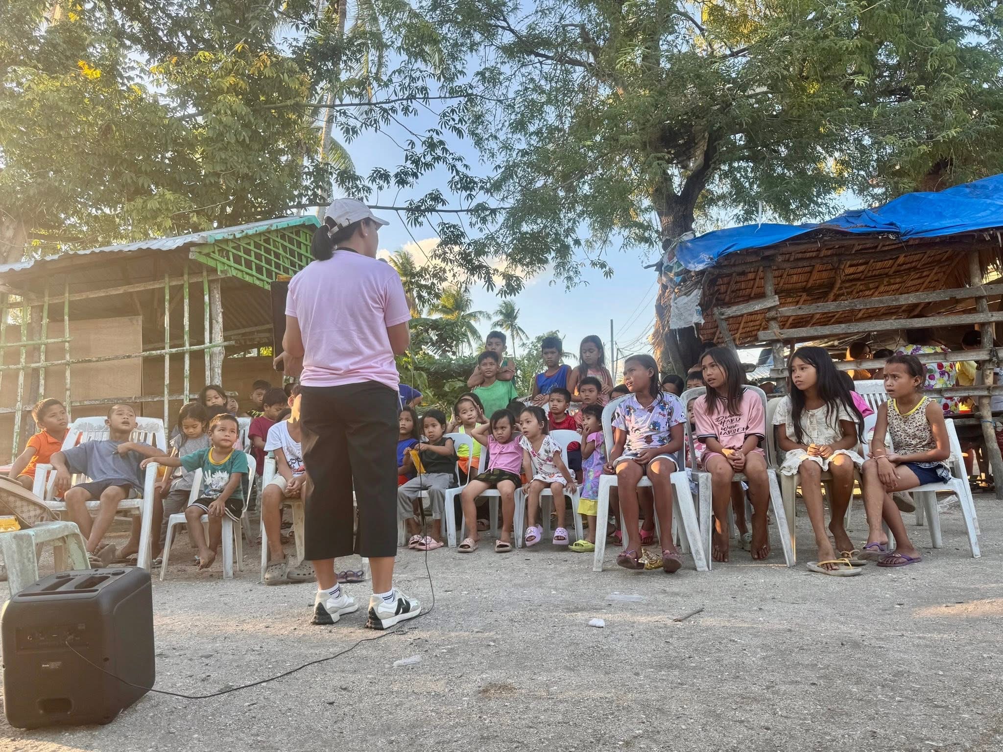 A teacher leads an outdoor Superkids Bible Club with children seated on chairs in a Masbate community